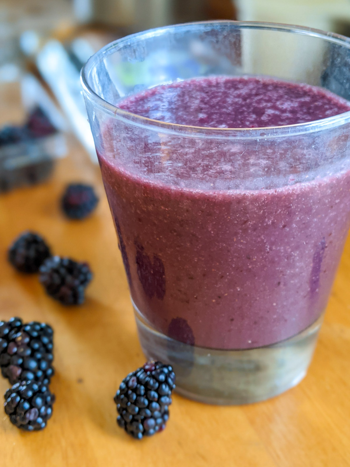 Purple blackberry smoothie in a glass with fresh blackberries on the counter.