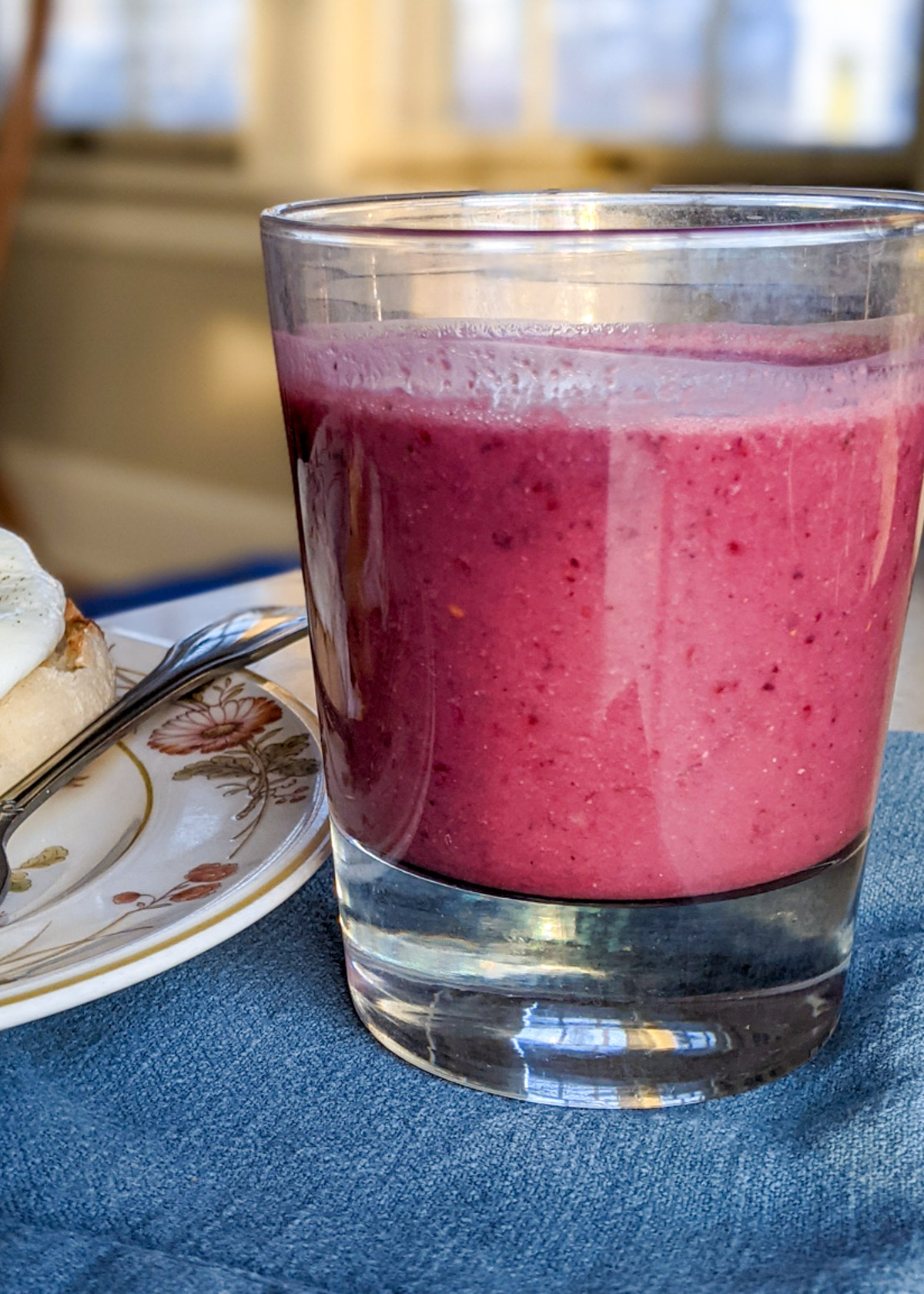 Protein mixed berry smoothie for breakfast on a blue napkin next to a plate of eggs.