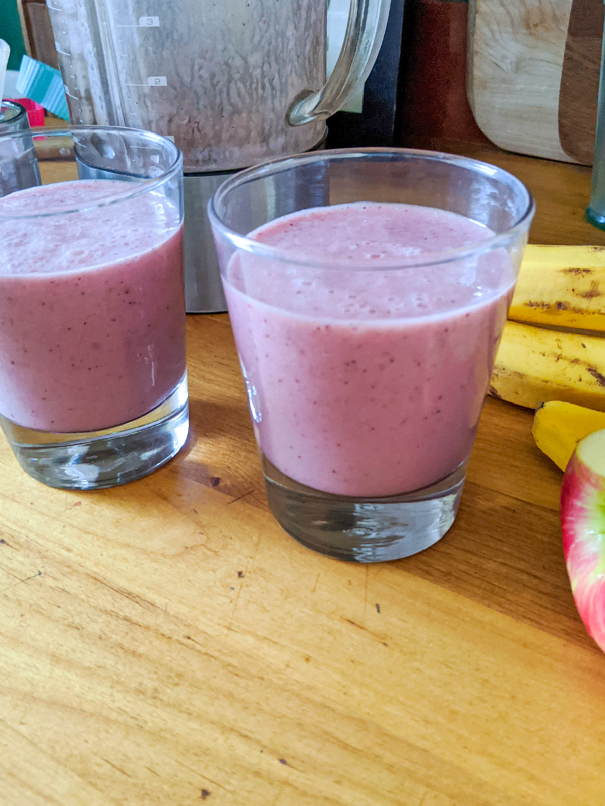 Smoothies made from leftover frozen fruit on the counter next to the blender, apple and banana.