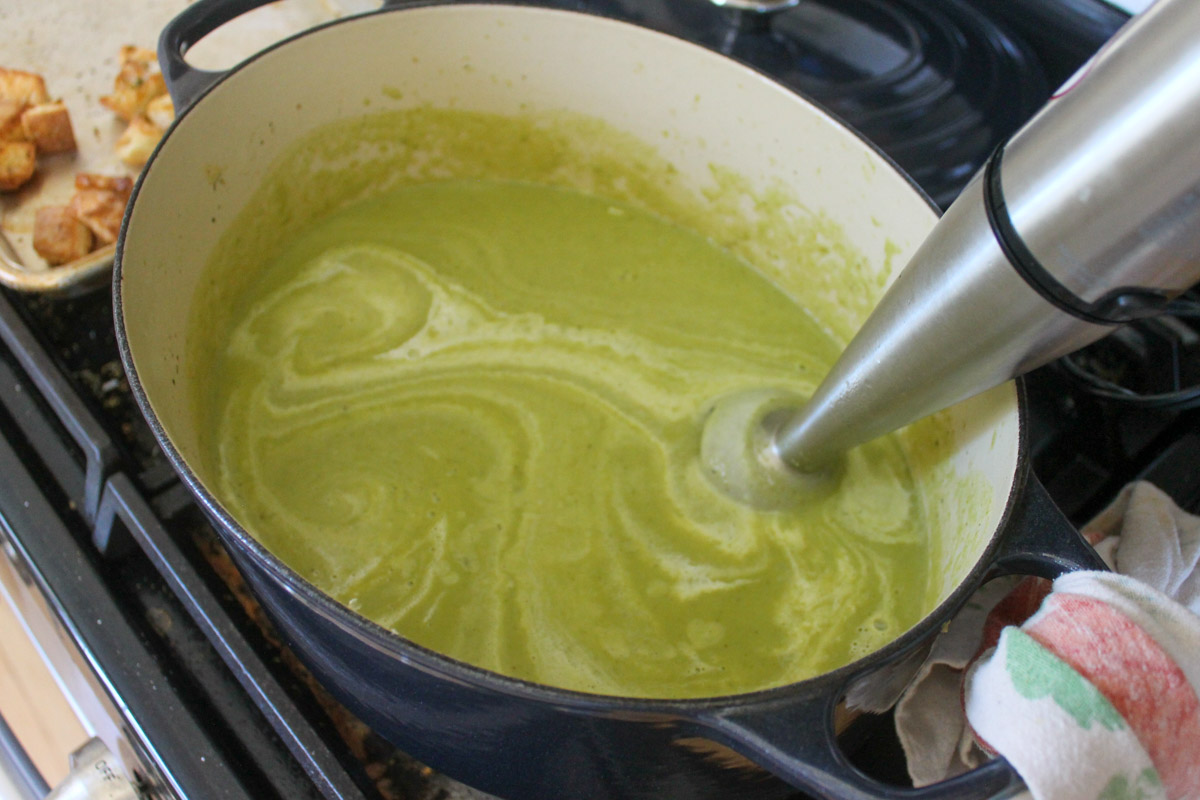 A pot of asparagus soup with cream being blended with an immersion blender.