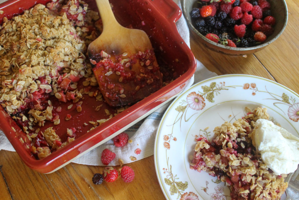 A plate of flourless rhubarb crisp with ice cream next to the pan of it and a bowl of berries.