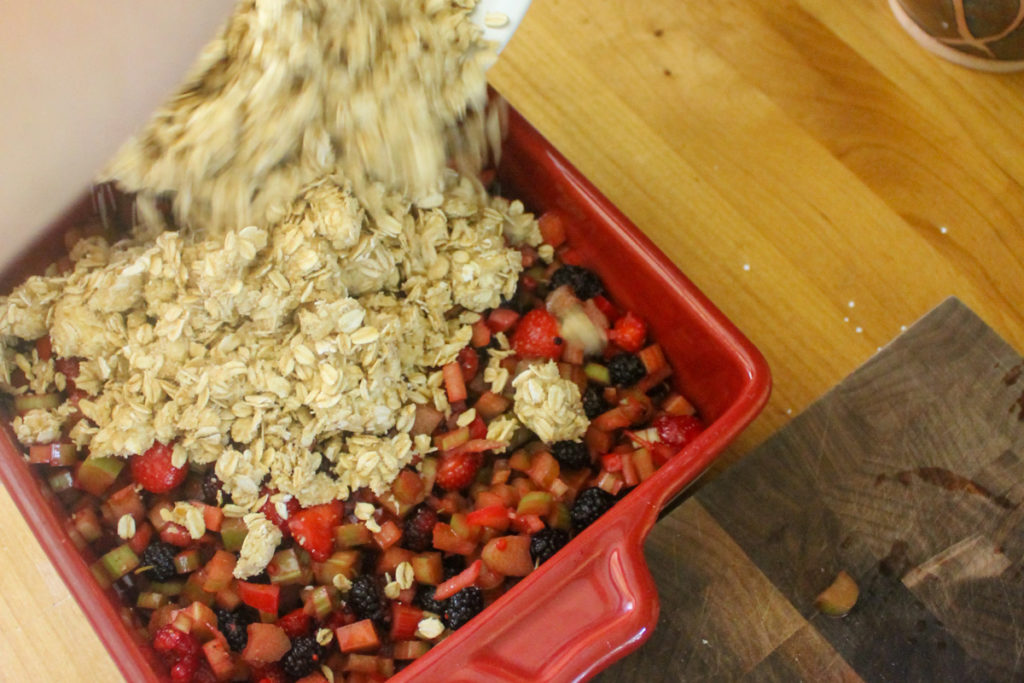 The process of pouring the oat topping onto the rhubarb berry filling.