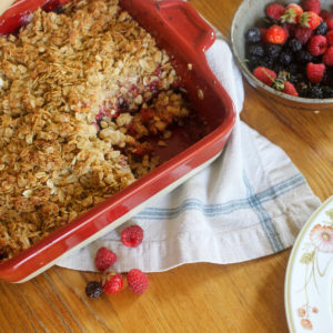 Berry Rhubarb Crisp with gluten free oat topping next to a bowl of mixed berries.