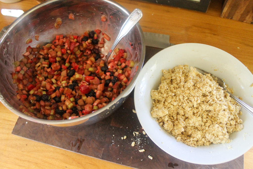 A bowl of berry rhubarb filling next to a bowl of gluten free oat topping.