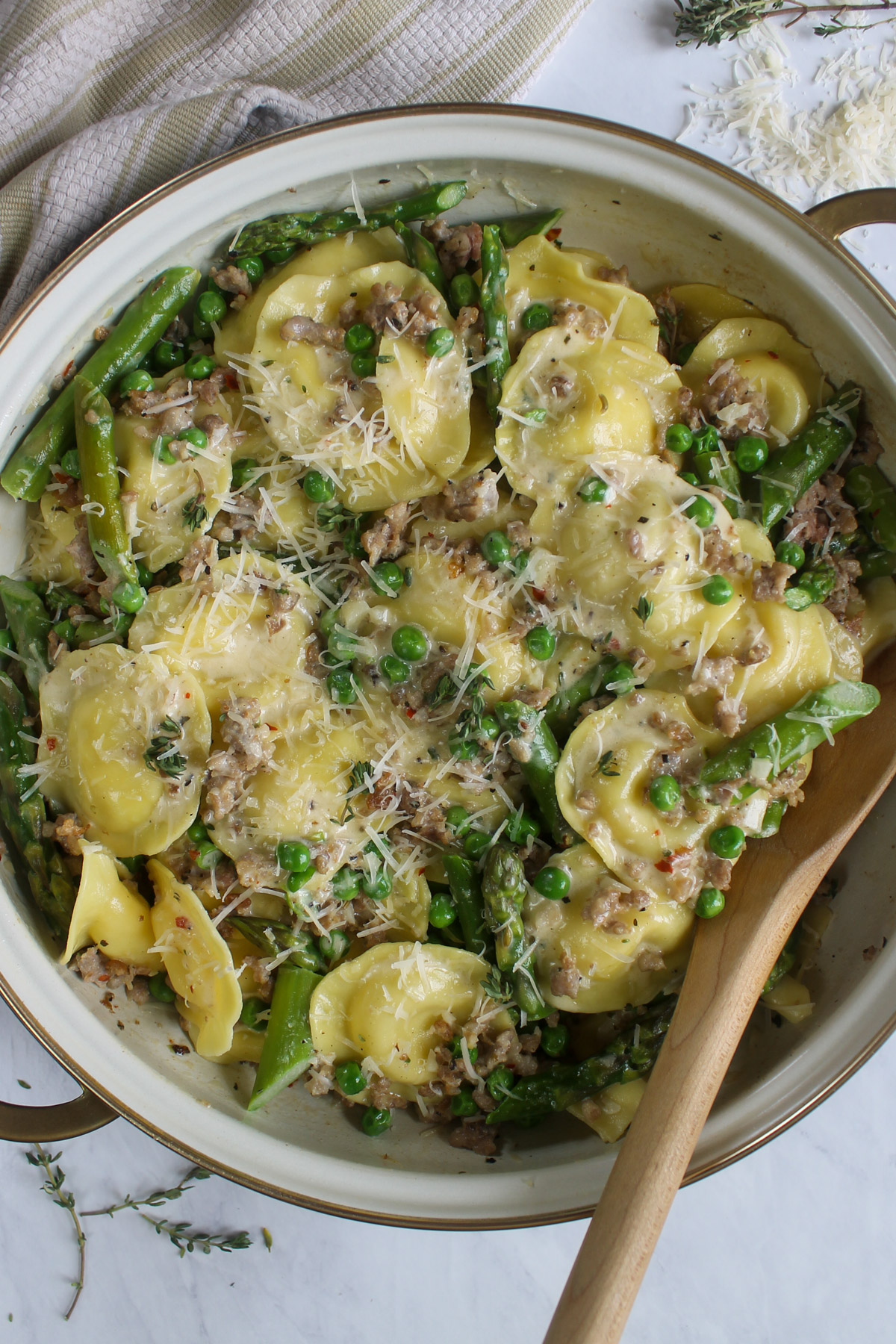 A gold rimmed skillet of Creamy Asparagus Ravioli with Sausage and Peas.