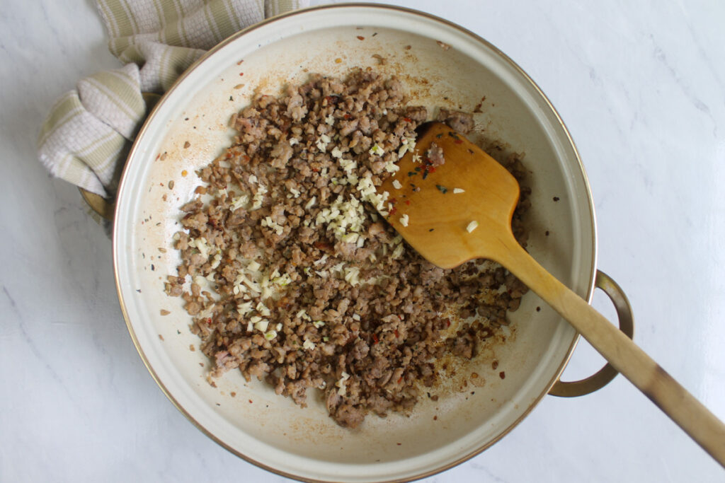 A pan of browning Italian sausage with garlic as the base for the ravioli cream sauce.