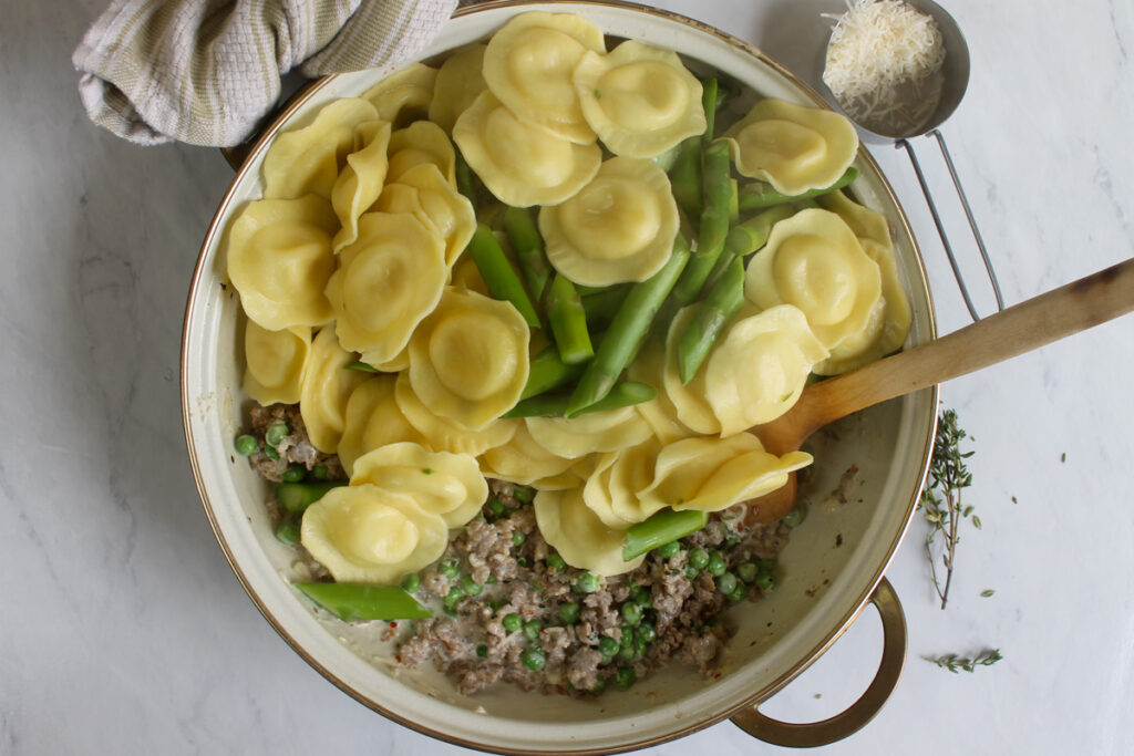 Combining the cooked ravioli and asparagus with the cream sauce.