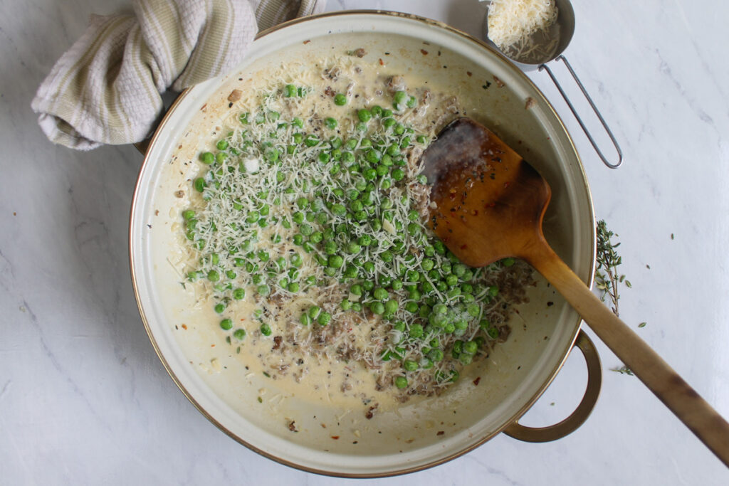 Ravioli cream sauce cooking with Italian sausage and peas.