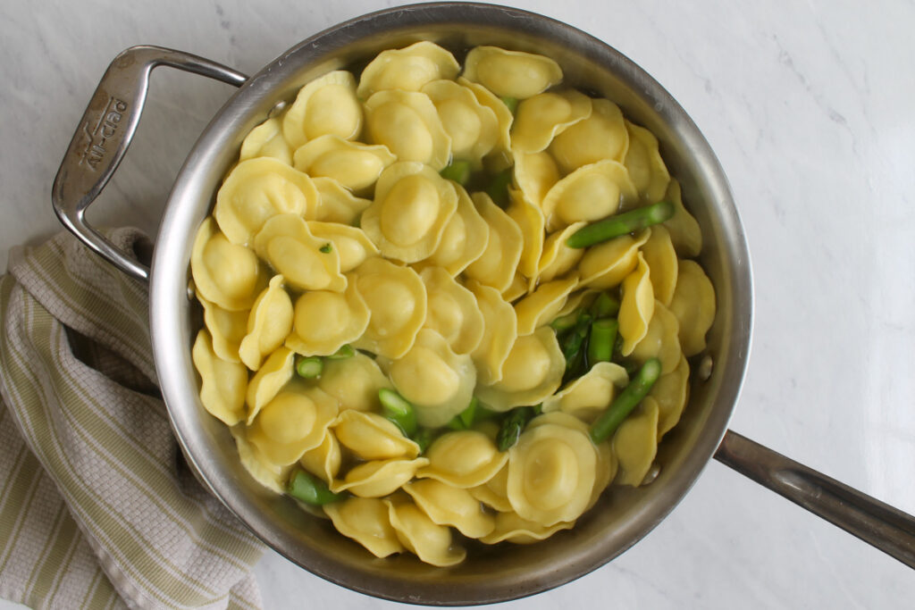 Cheese ravioli and asparagus boiling together in a large pot or water.