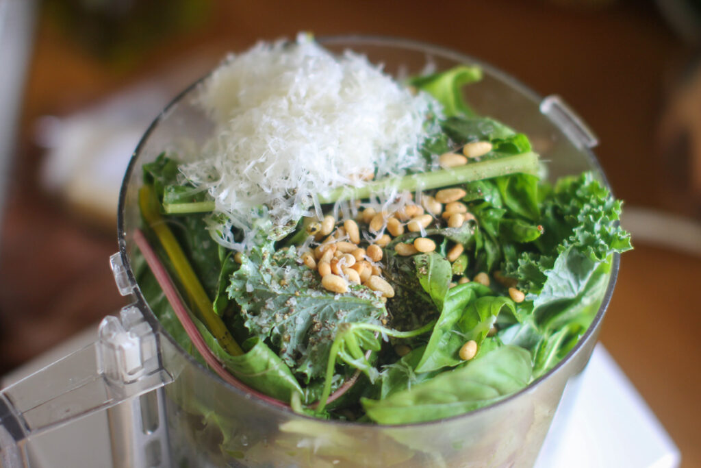 A food processor of greens, basil, pine nuts, and Parmesan ready to make pesto aioli.