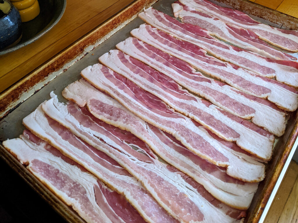 Bacon ready to cook on a sheet pan in the oven.