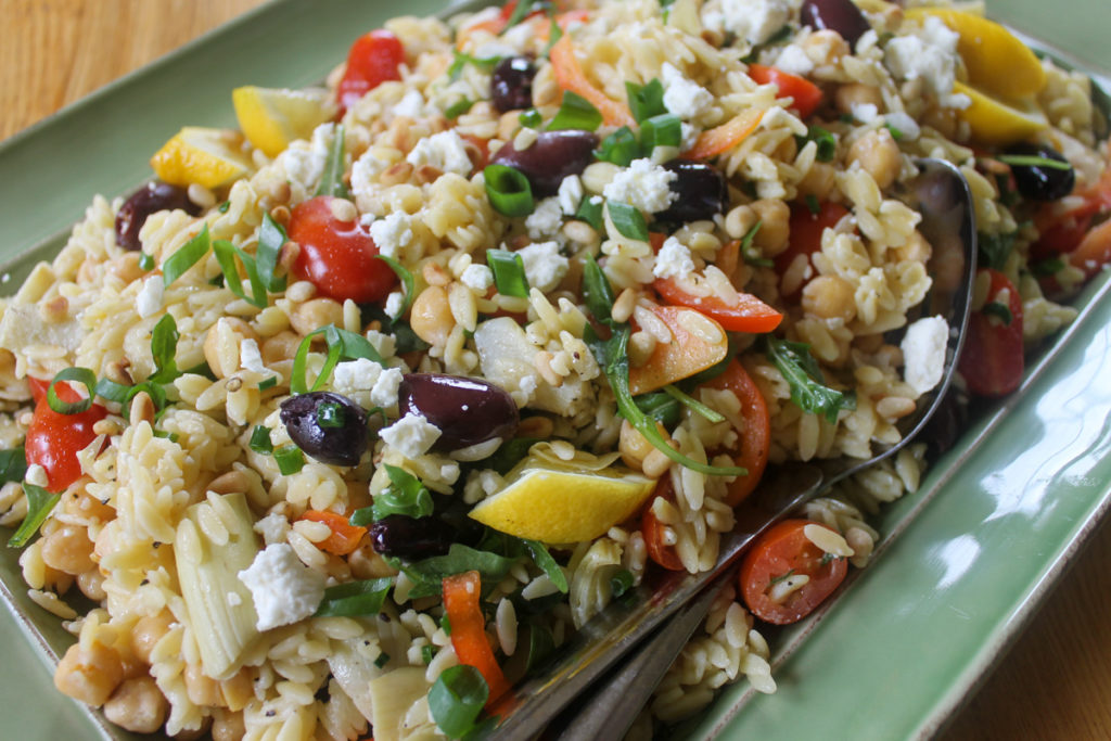 A green platter of lemon orzo pasta salad with kalamata olives, tomato, feta and arugula.