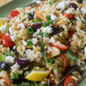 Platter of orzo pasta salad with lemon, cherry tomatoes and chickpeas.
