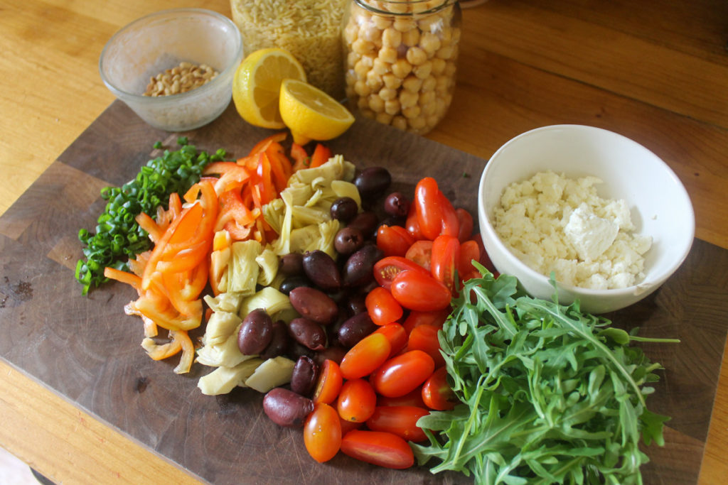 Lemon orzo pasta salad ingredients chopped on a cutting board.