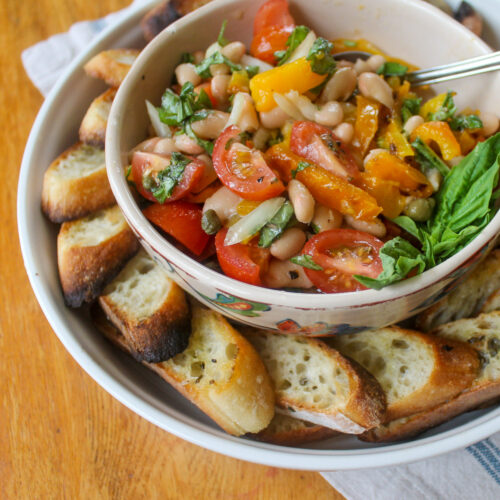Bowl of white bean bruschetta surrounded by a plate of toasted crostini bread.