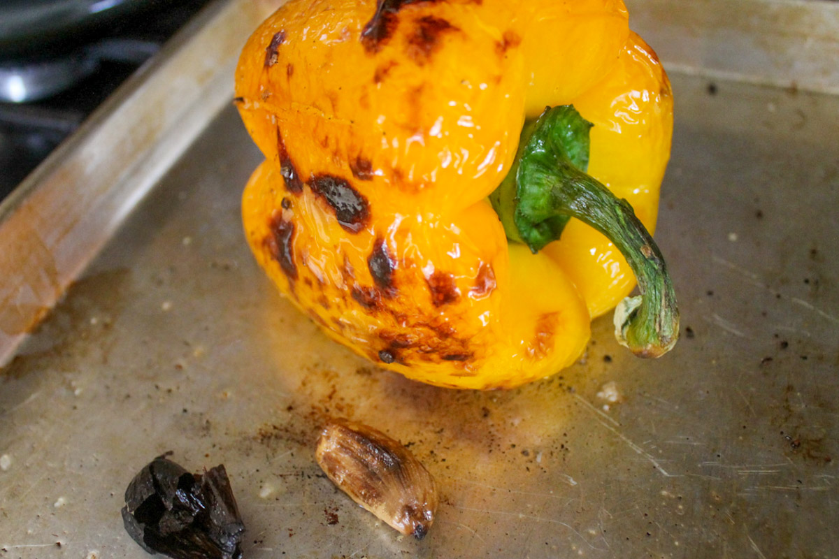 A roasted yellow bell pepper and garlic clove on a sheet pan.
