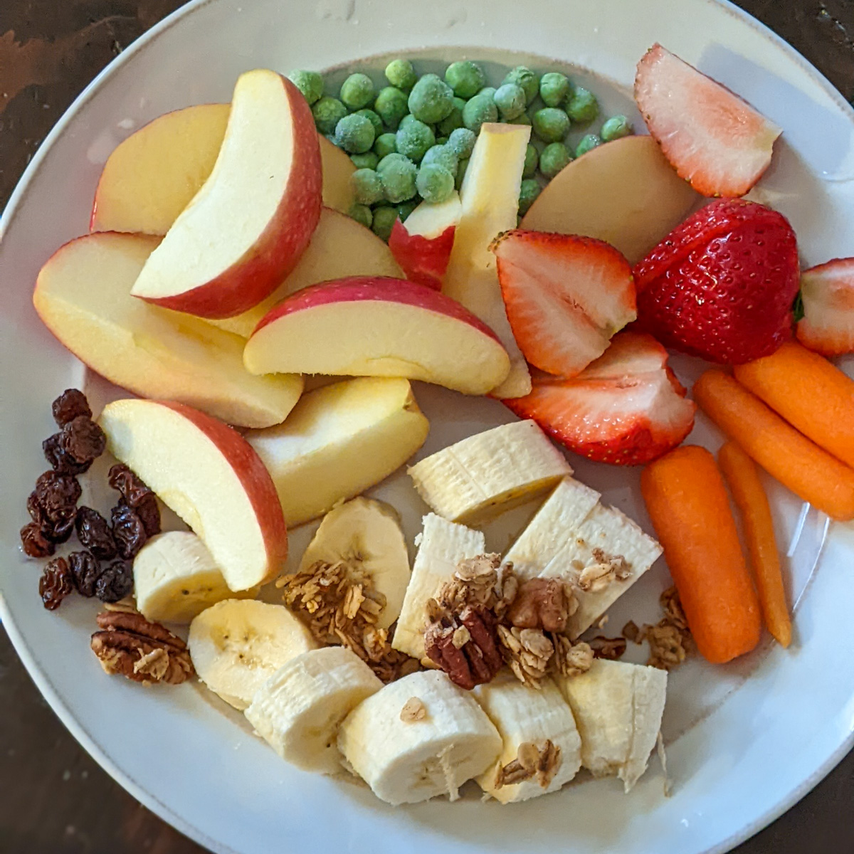 A Healthy bedtime kid's snack with apples, banana and granola, carrots, strawberries, raisins and peas.