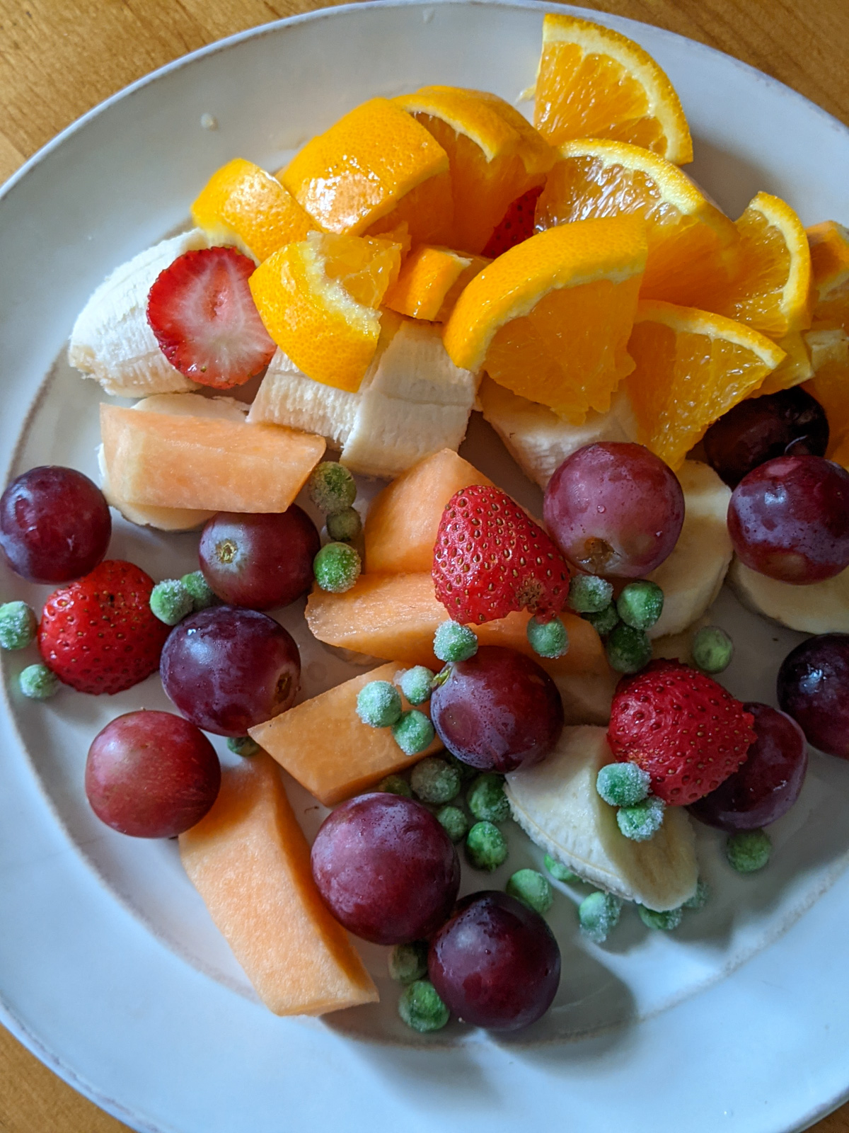 Healthy snacks to share like oranges, melon, grapes, banana, strawberry and peas.
