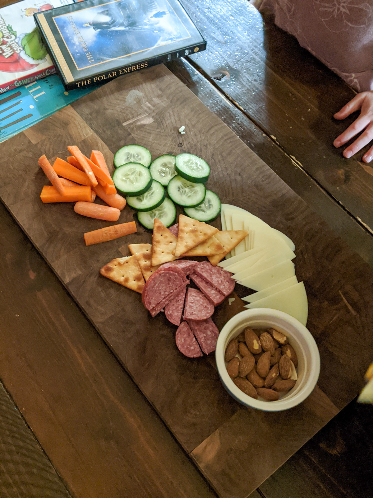 Bedtime snacks on a cutting board, salami, cucumber, carrots, cheese, pita crackers and a bowl of nuts.