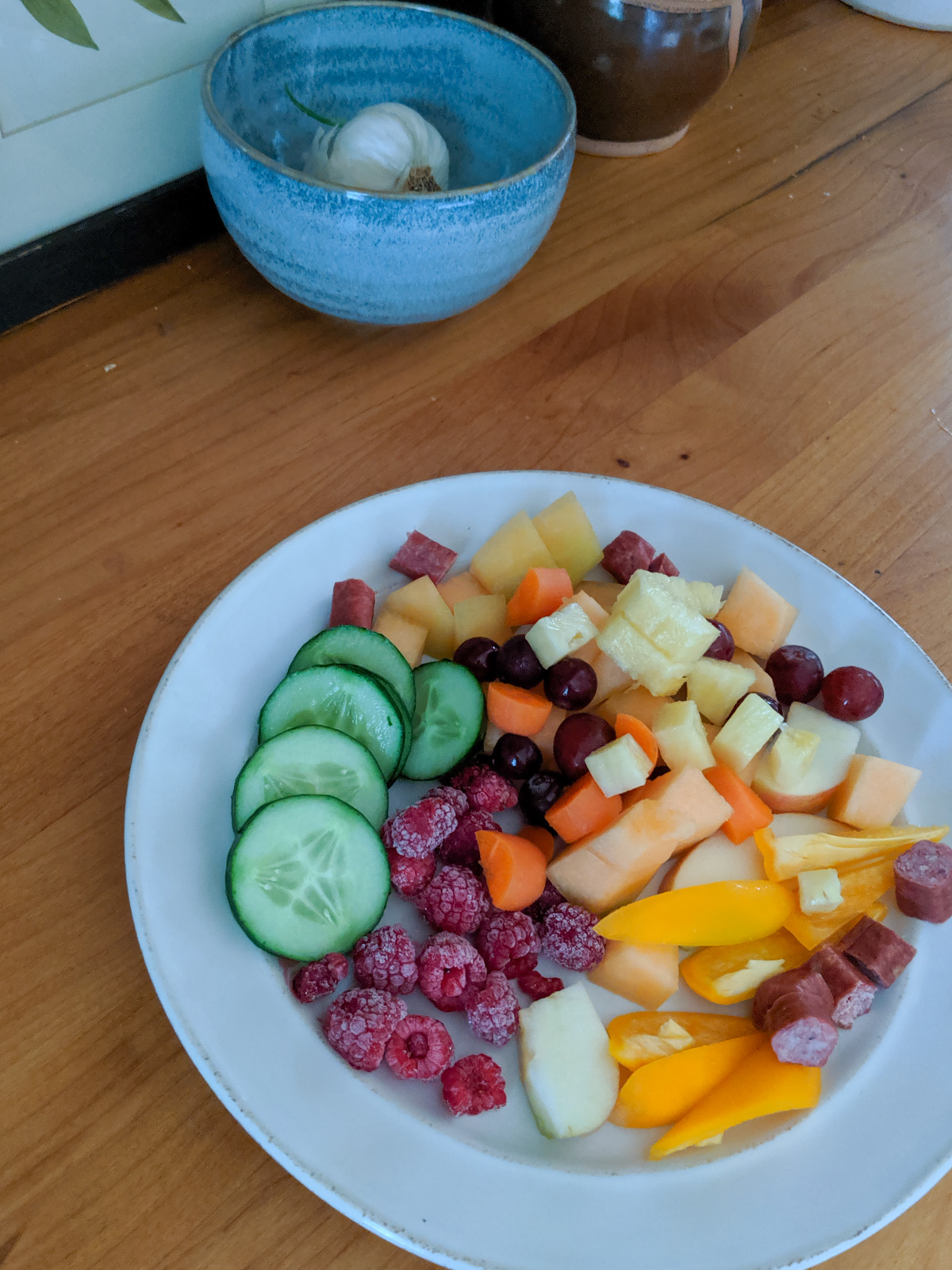 A plate of bedtime snacks for kids with cucumber, raspberry, pineapple, beef sticks and bell pepper.