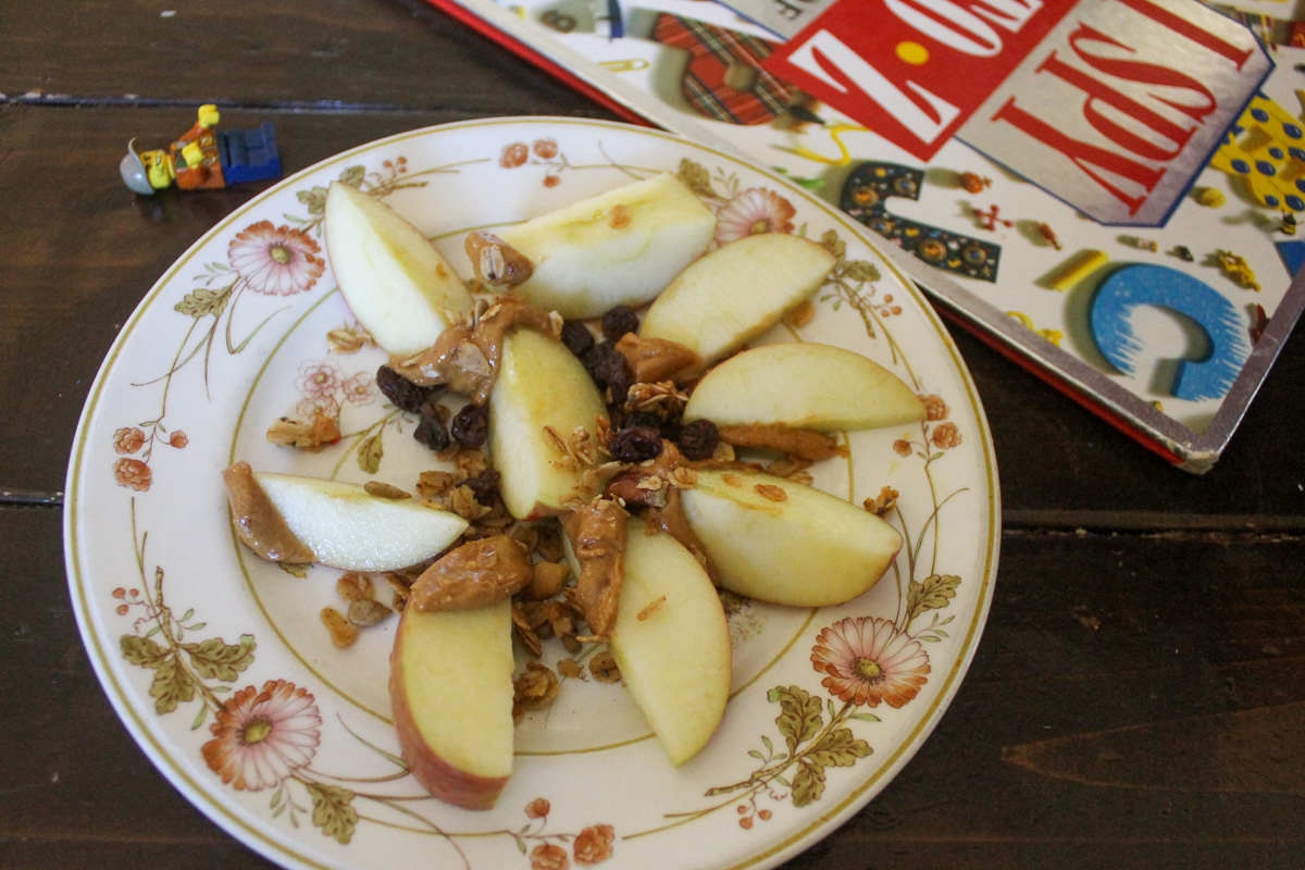 A plate of sliced apples dipped in peanut butter and sprinkled with granola and raisins.