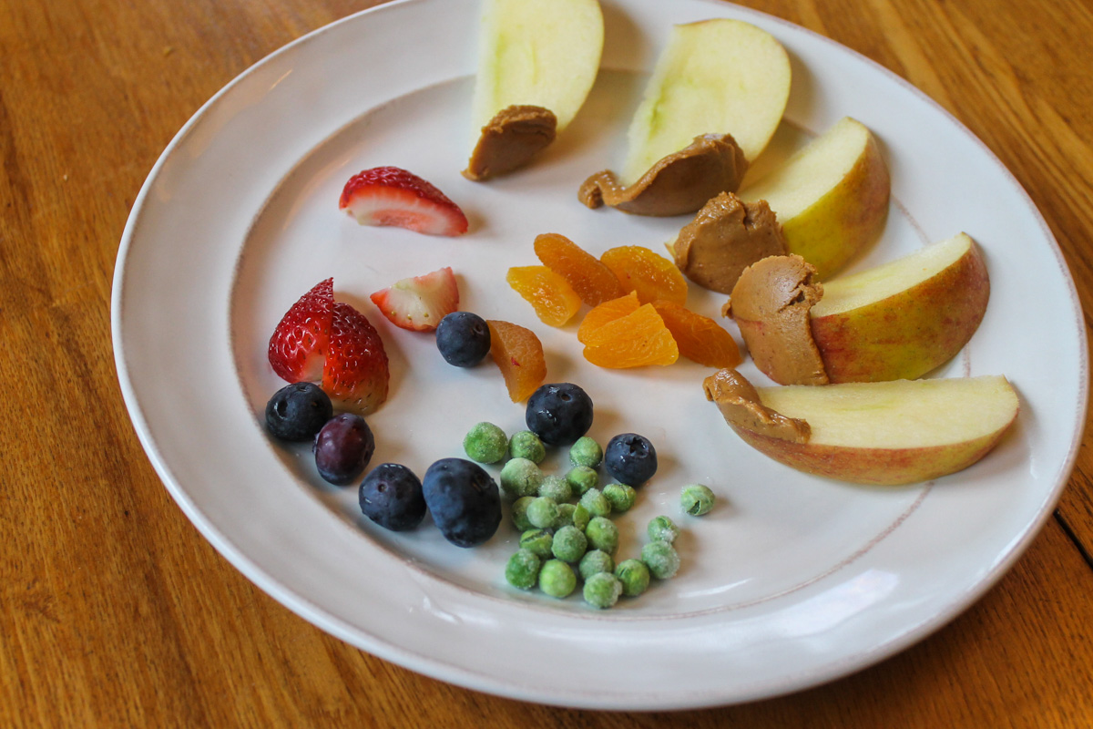 A healthy kid's snack with apples dipped in peanut butter, berries and frozen peas.