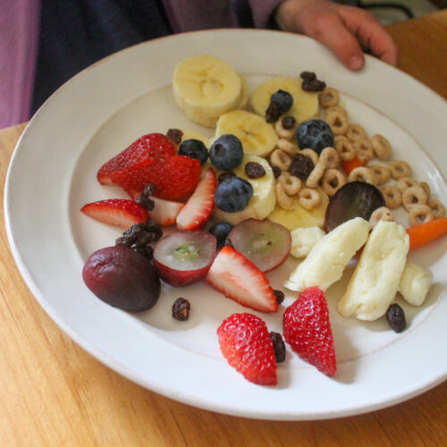 Kids bedtime snacks on a plate with fruit, cheese curds and cereal.