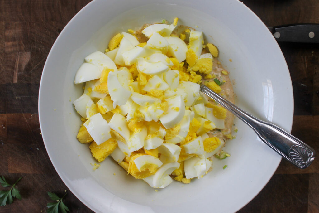 Adding the chopped hard boiled eggs to the bowl with the dressing ingredients.