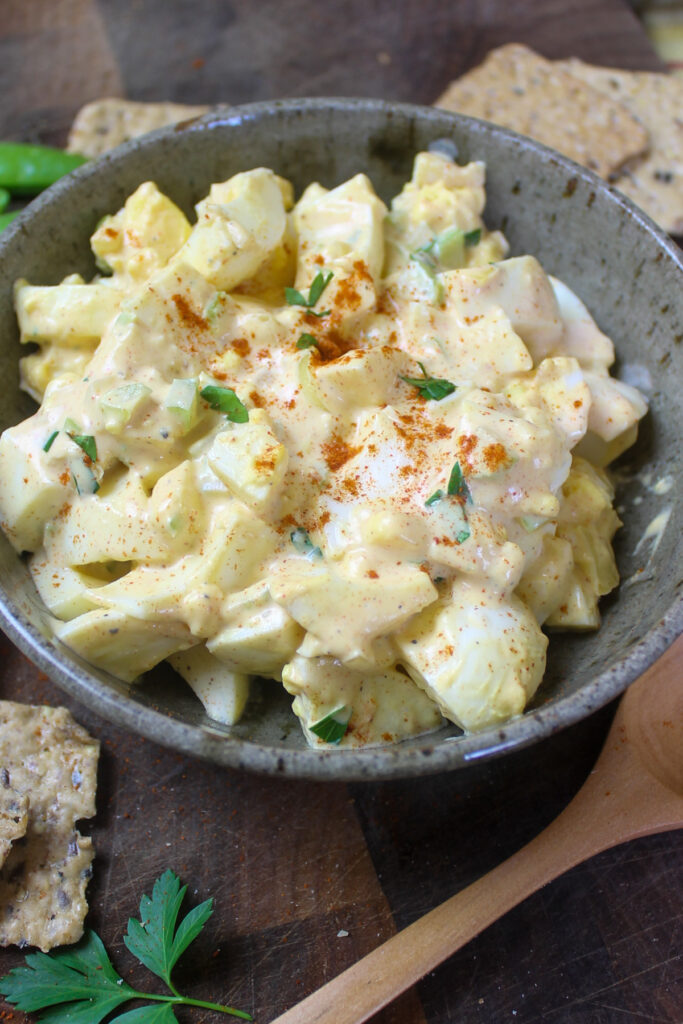 A bowl of egg salad with crackers to dip.