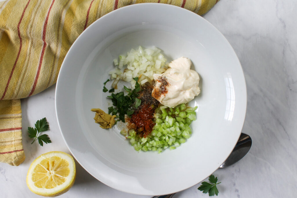 Bowl of ingredients for egg salad, onion, celery, dijon, mayo, herbs, lemon and seasonings.