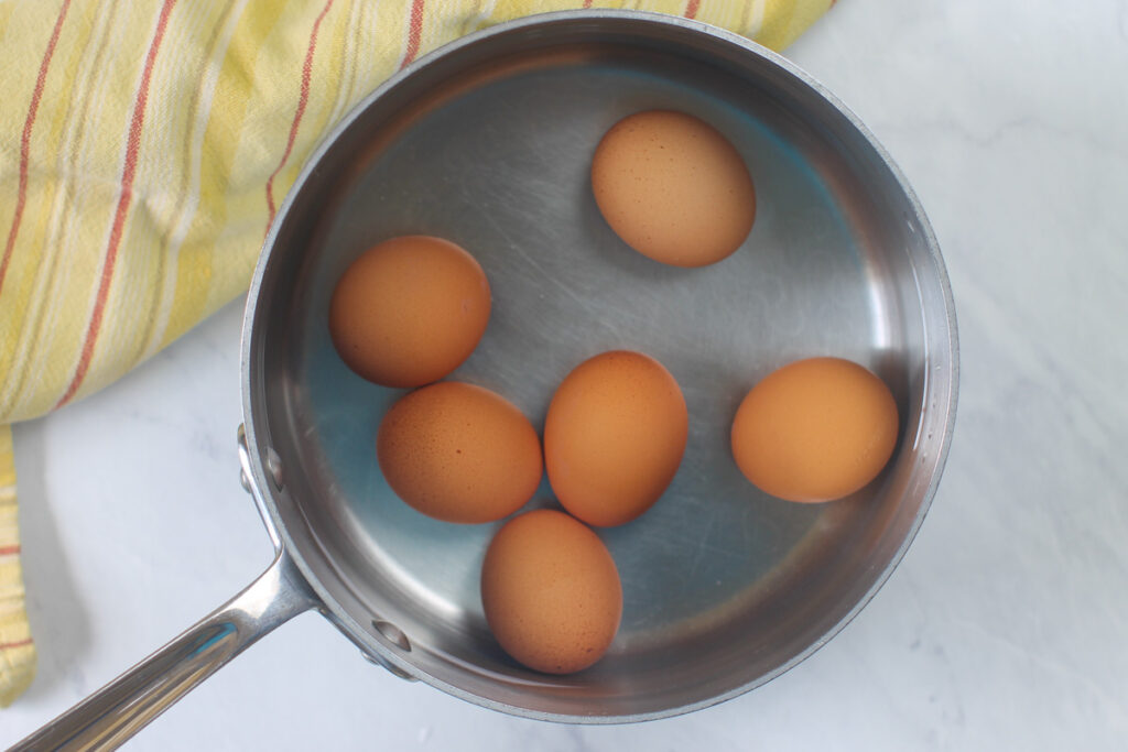 A pot of 6 raw eggs ready to hard boil in water.