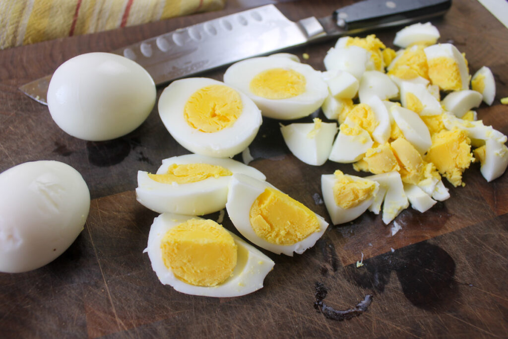 Perfectly cooked hard boiled eggs being chopped on a cutting board.