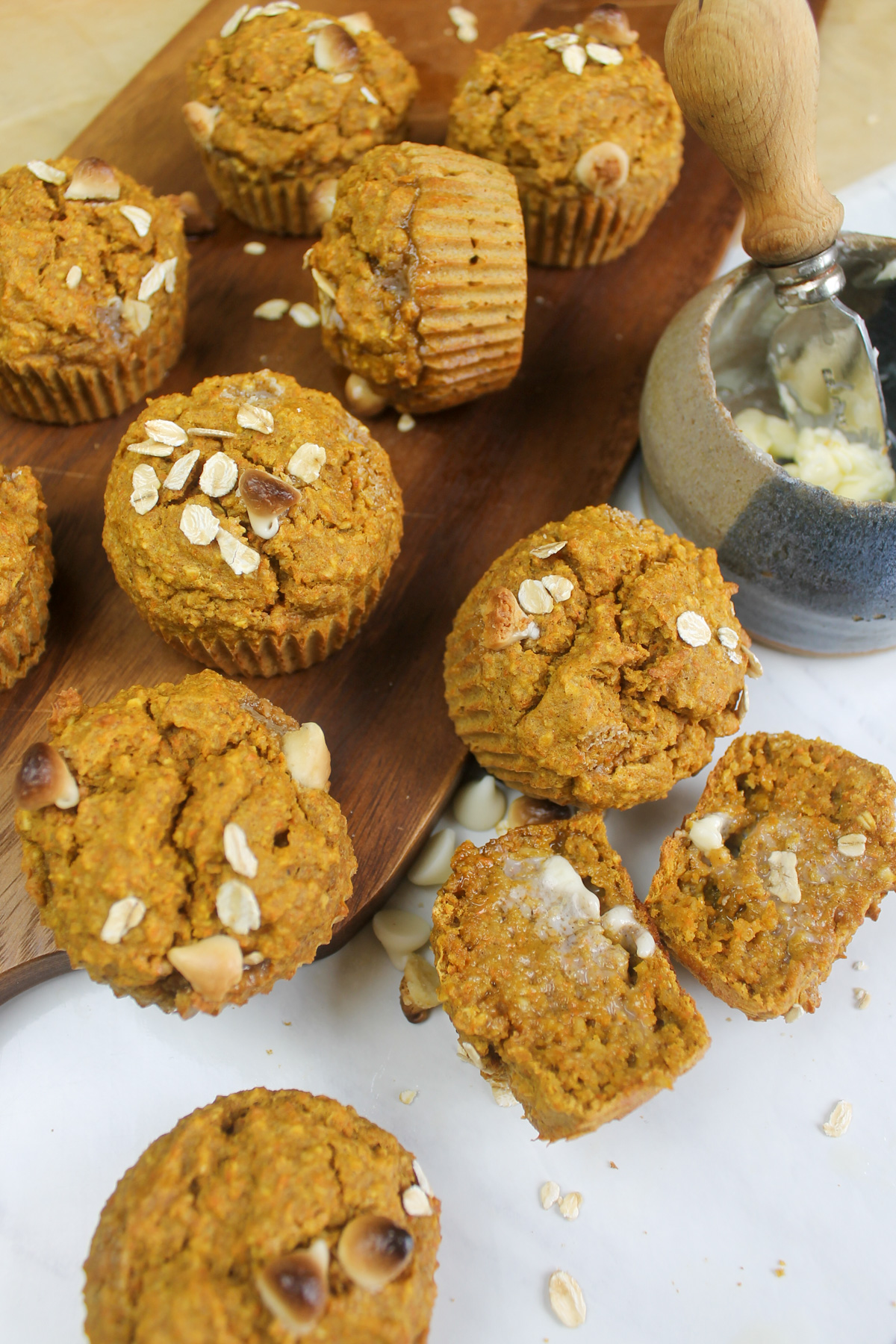 Banana Carrot Muffins on a cutting board and white countertop with a dish of butter.