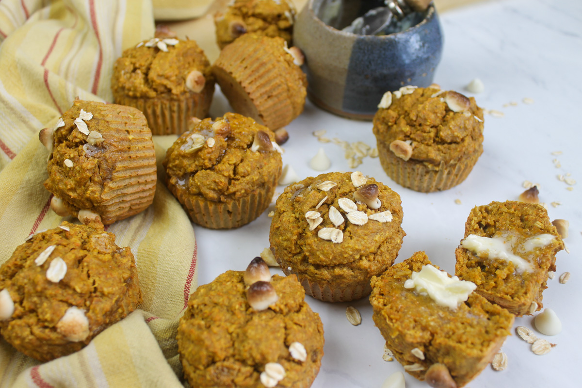 Carrot Banana Oatmeal Muffins on a white surface with oats and white chocolate chips.