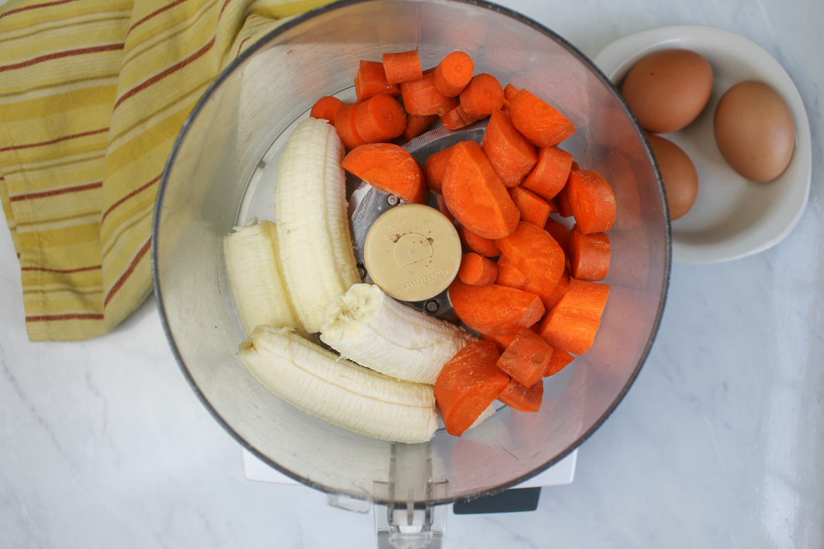 Bananas and chopped carrots in the bowl of a food processor ready to puree.