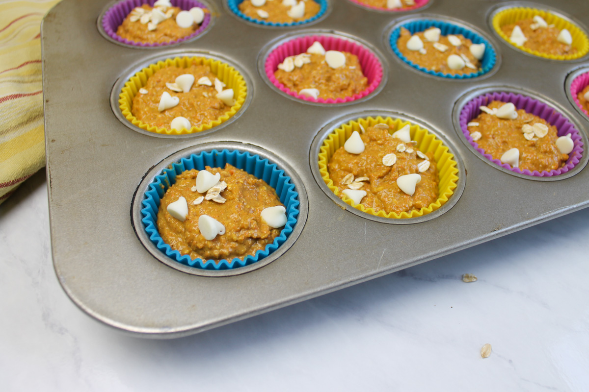 Lined silicone muffin cups filled with batter and topped with white chocolate chips and oats.
