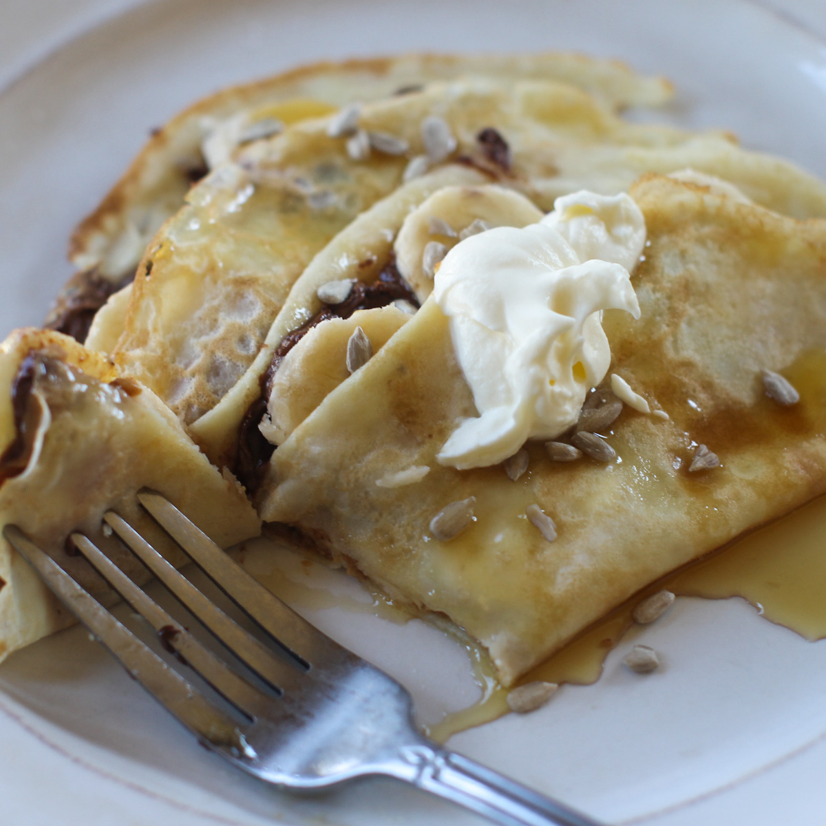 Crepes filled with Nutella and sliced banana, folded over and topped with whipped cream, sunflower seeds and maple syrup.