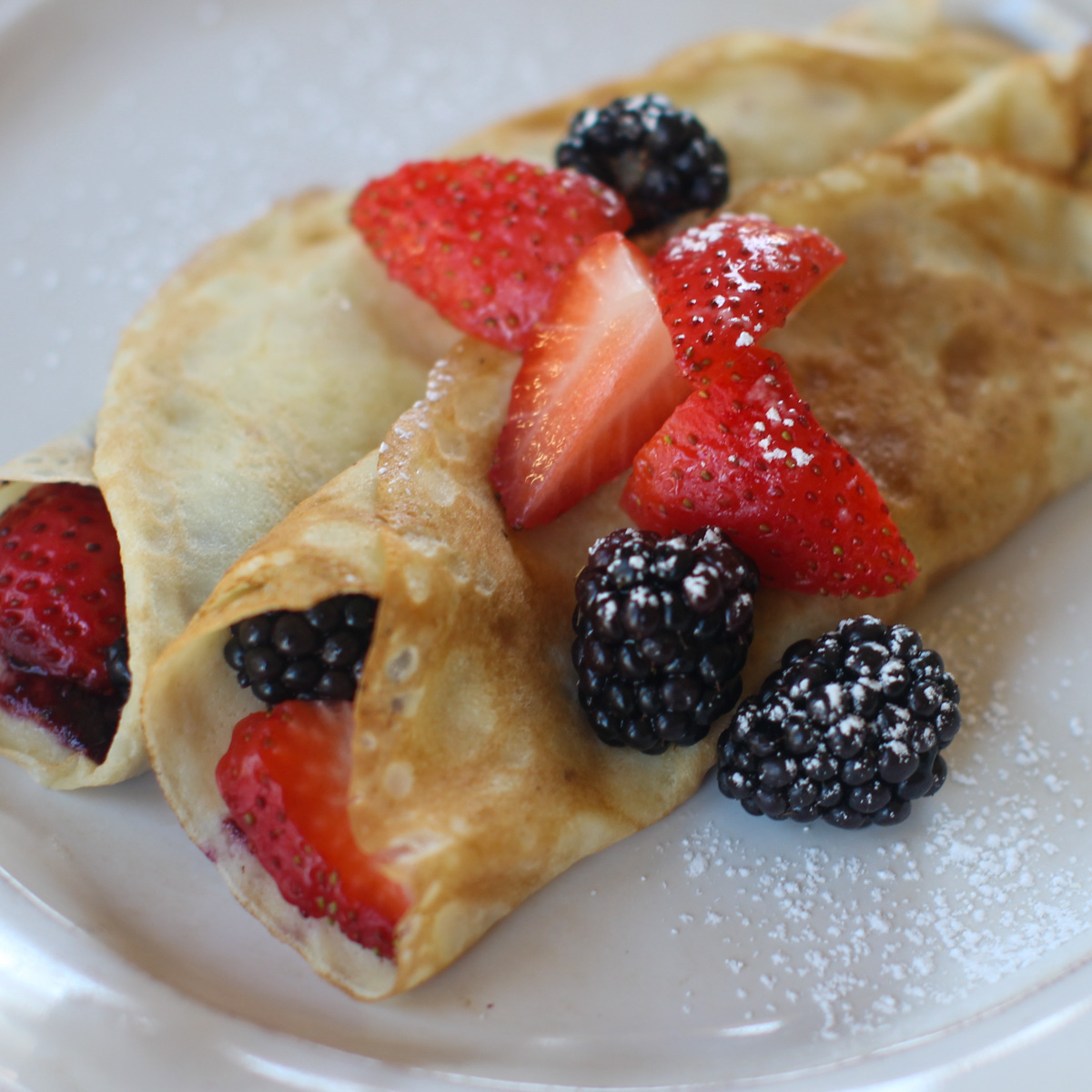 Strawberry and Blackberry rolled into crepes and more on top with powdered sugar.