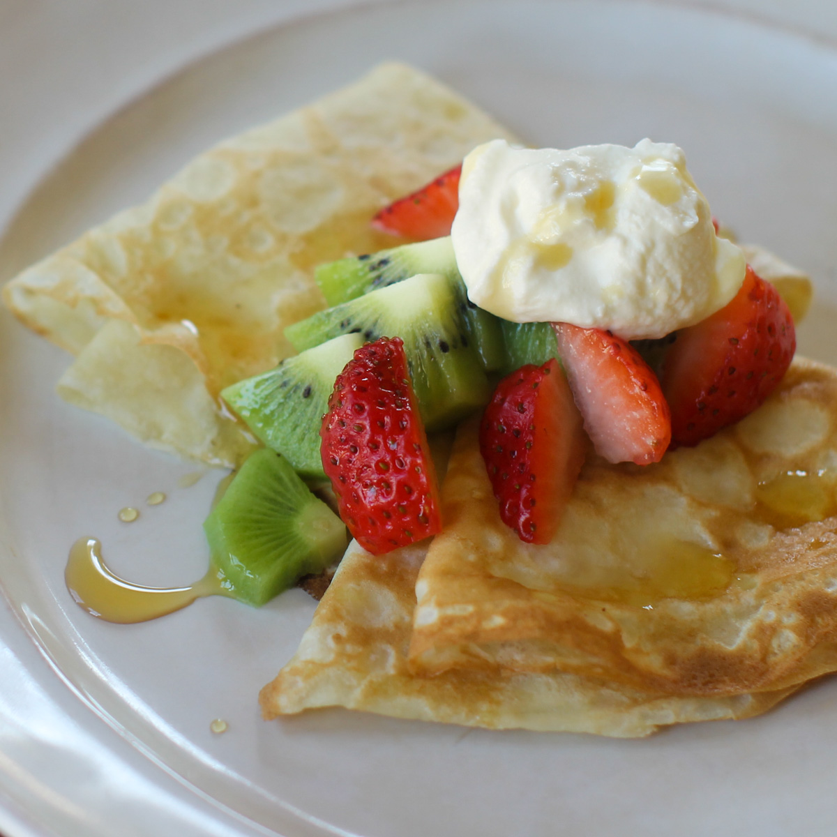 Crepes folded and topped with strawberry, kiwi, fresh whipped cream and a drizzle of maple syrup.