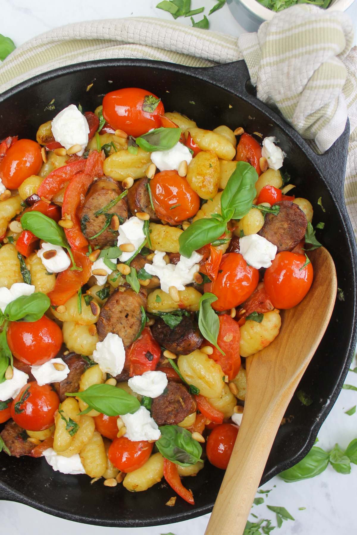 Pan fried gnocchi with spinach, tomato, peppers and Italian sausage links with a wooden spoon.