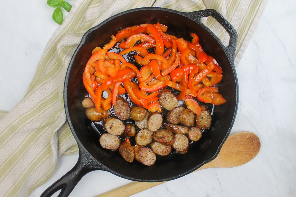 Red bell pepper and sausage sautéing in a cast iron skillet.