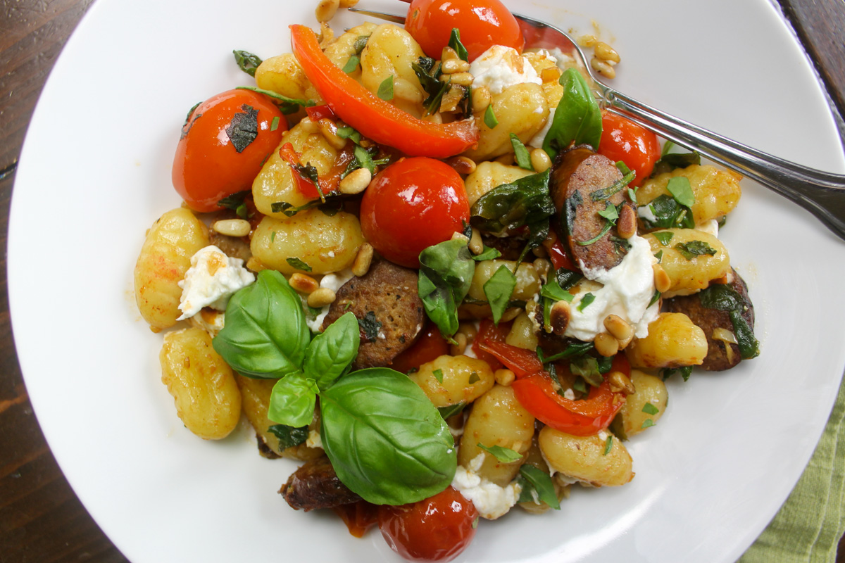 Gnocchi with Italian sausage, burst tomatoes, goat cheese and basil on a white plate.