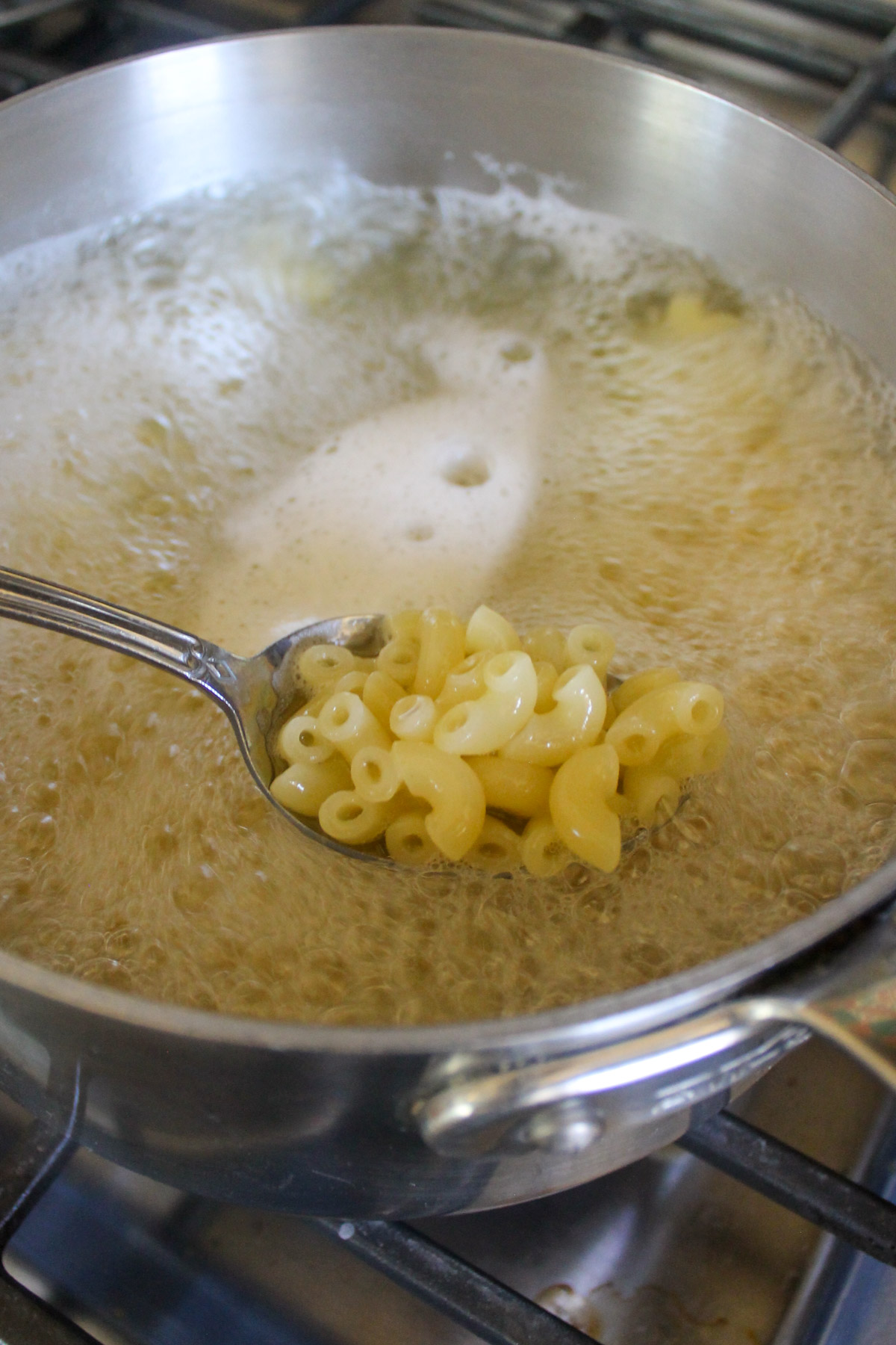 Macaroni pasta boiling in water with a spoon scooping some.