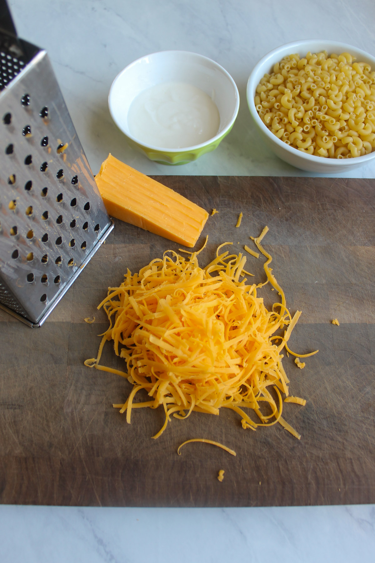 Shredded cheddar cheese on a cutting board with a box grater.
