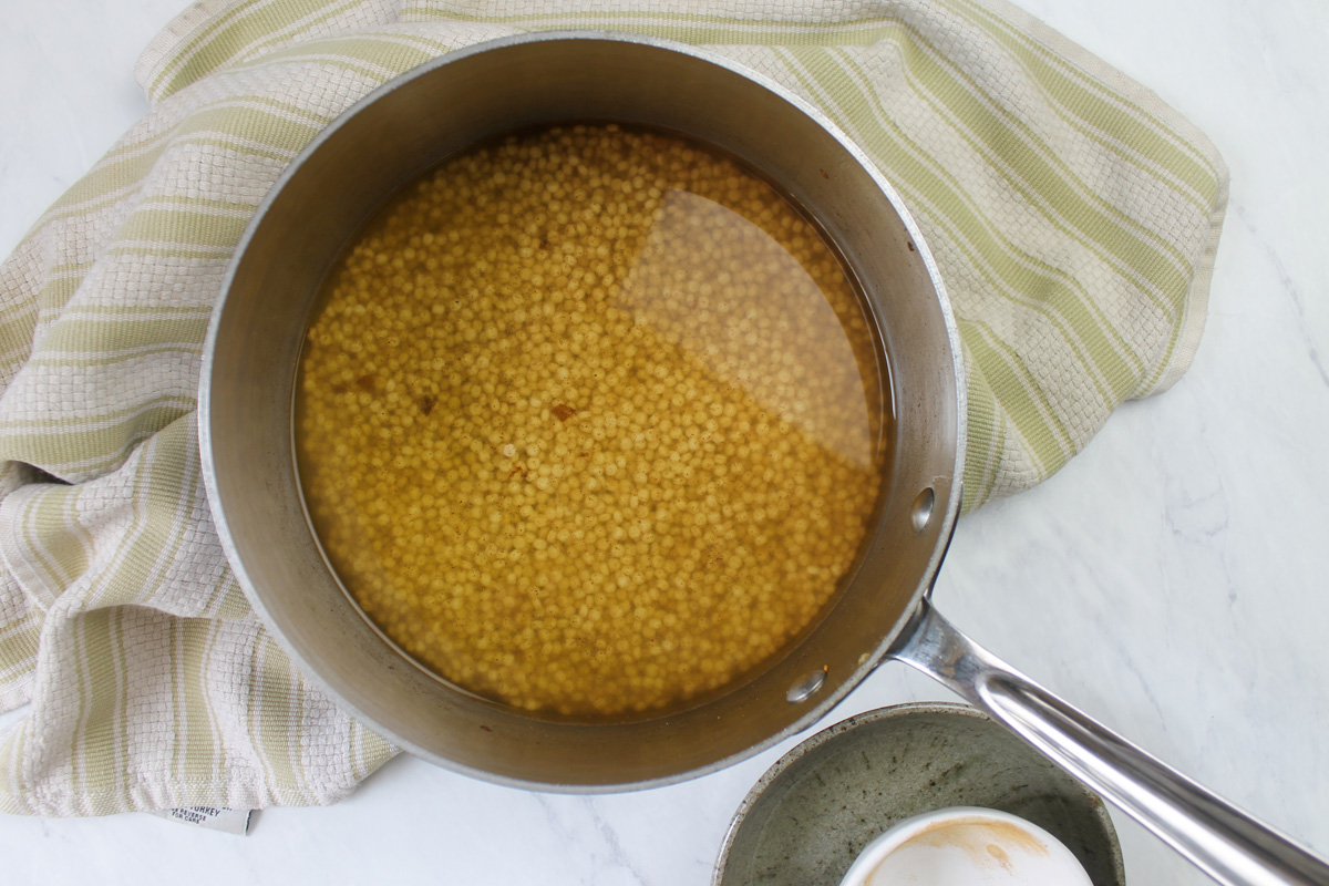 A pot of raw couscous in chicken stock ready to simmer.