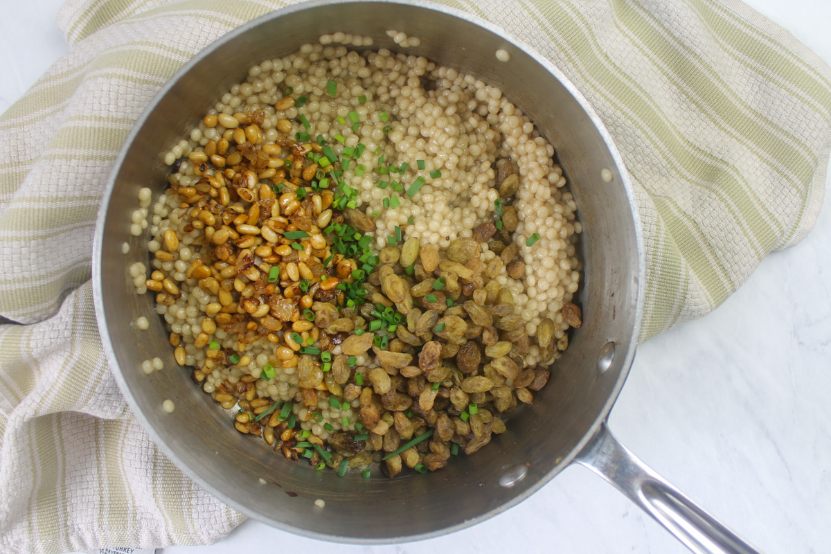 Adding onion, pine nuts, golden raisins and chives to cooked couscous.