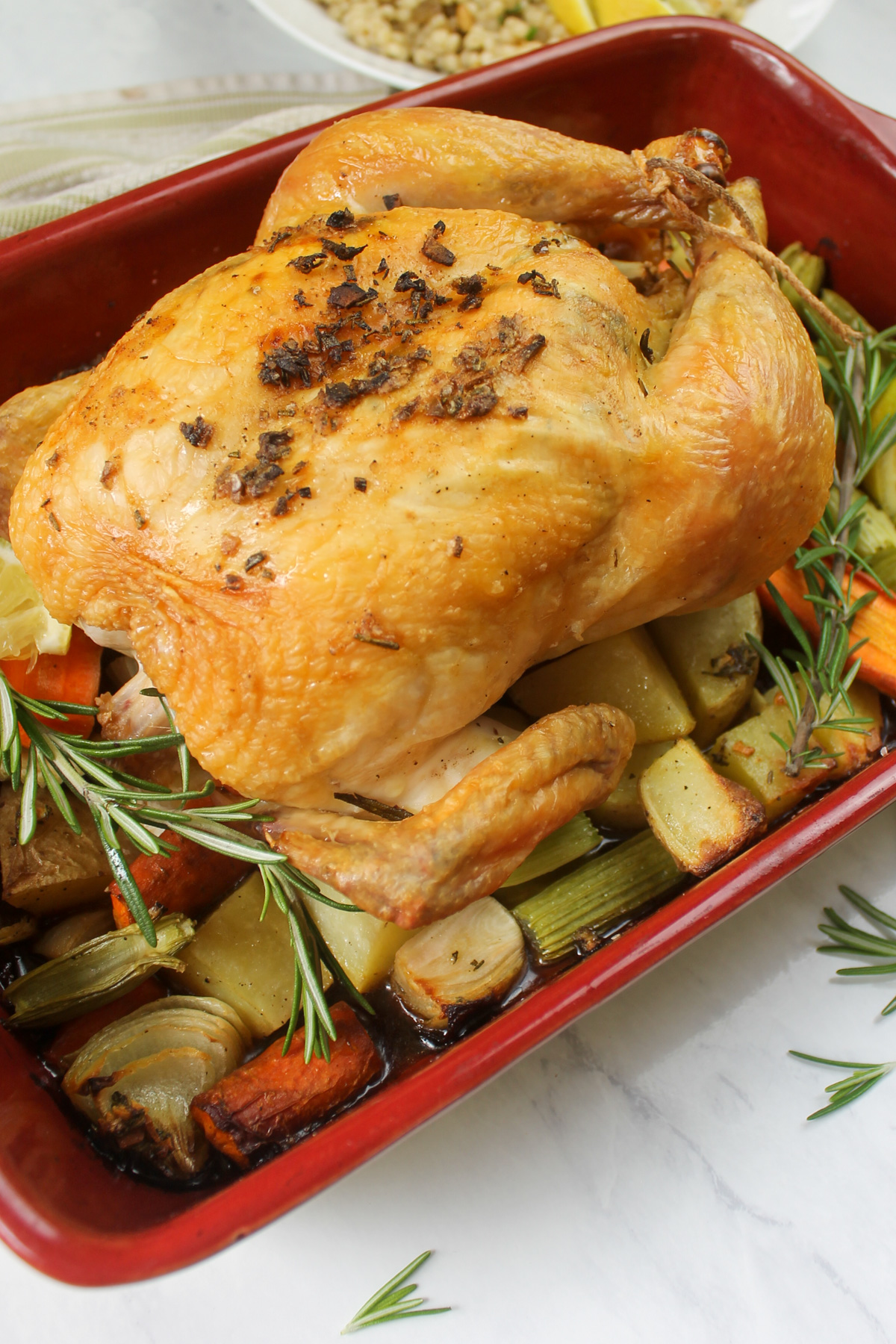 The finished whole roasted chicken in a red casserole dish on top of veggies.