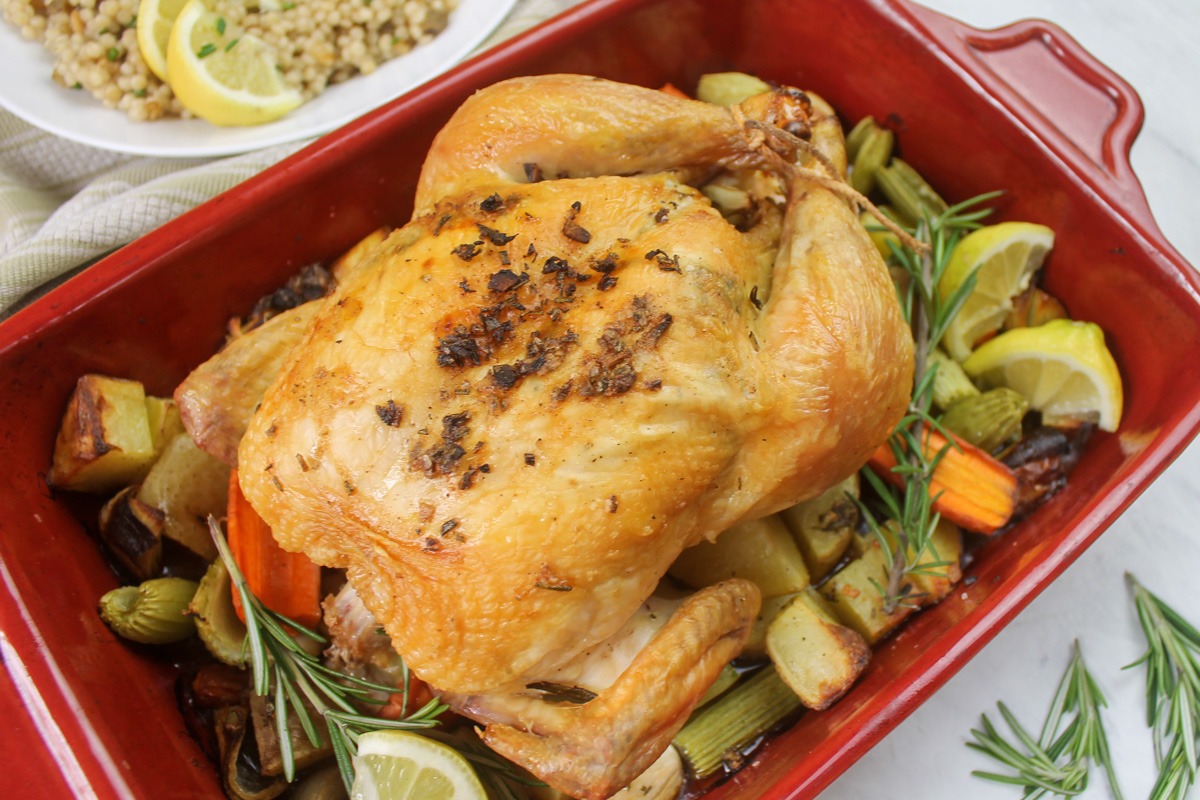 Crispy roasted chicken on vegetables with sprigs of rosemary.