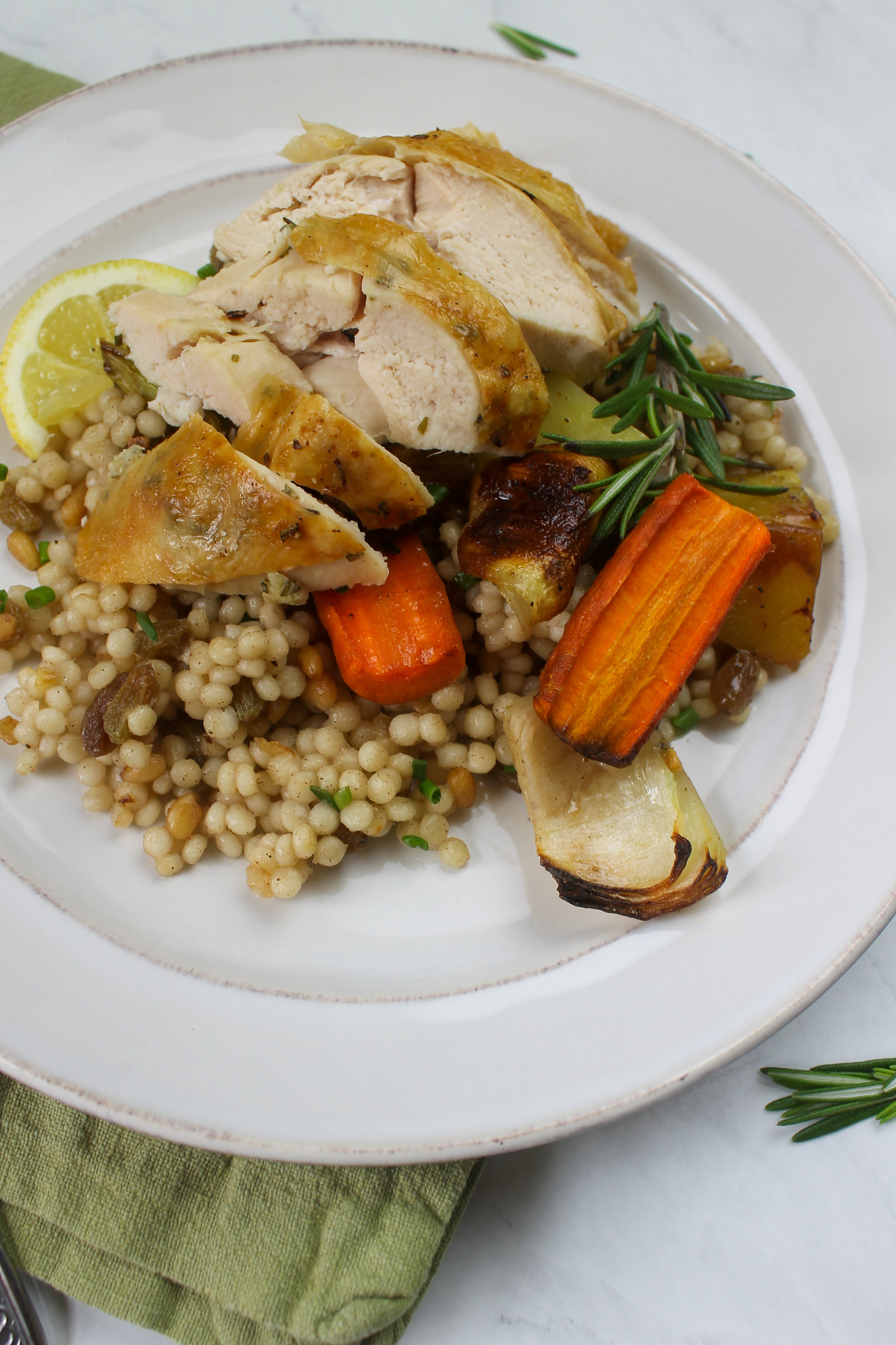 A plate of couscous topped with sliced chicken and root vegetables.