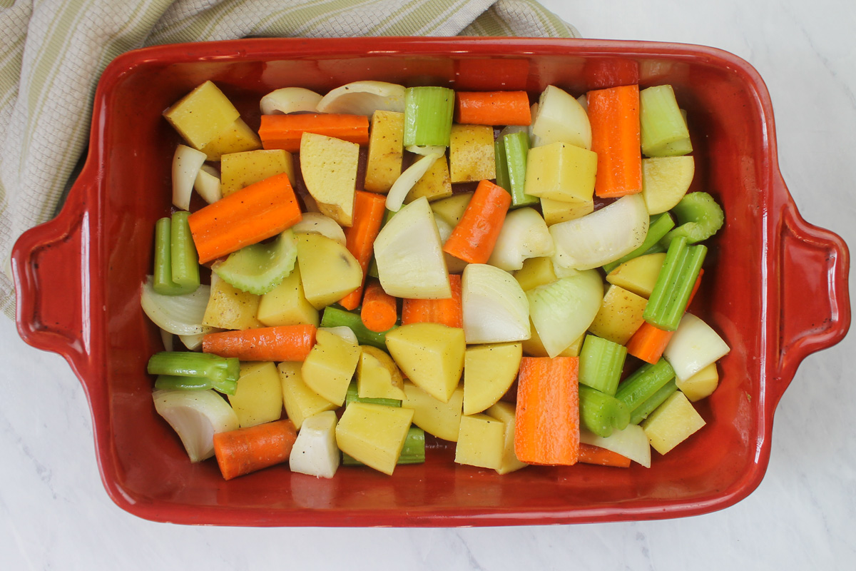 A red casserole pan filled with root vegetables ready to roast with chicken.